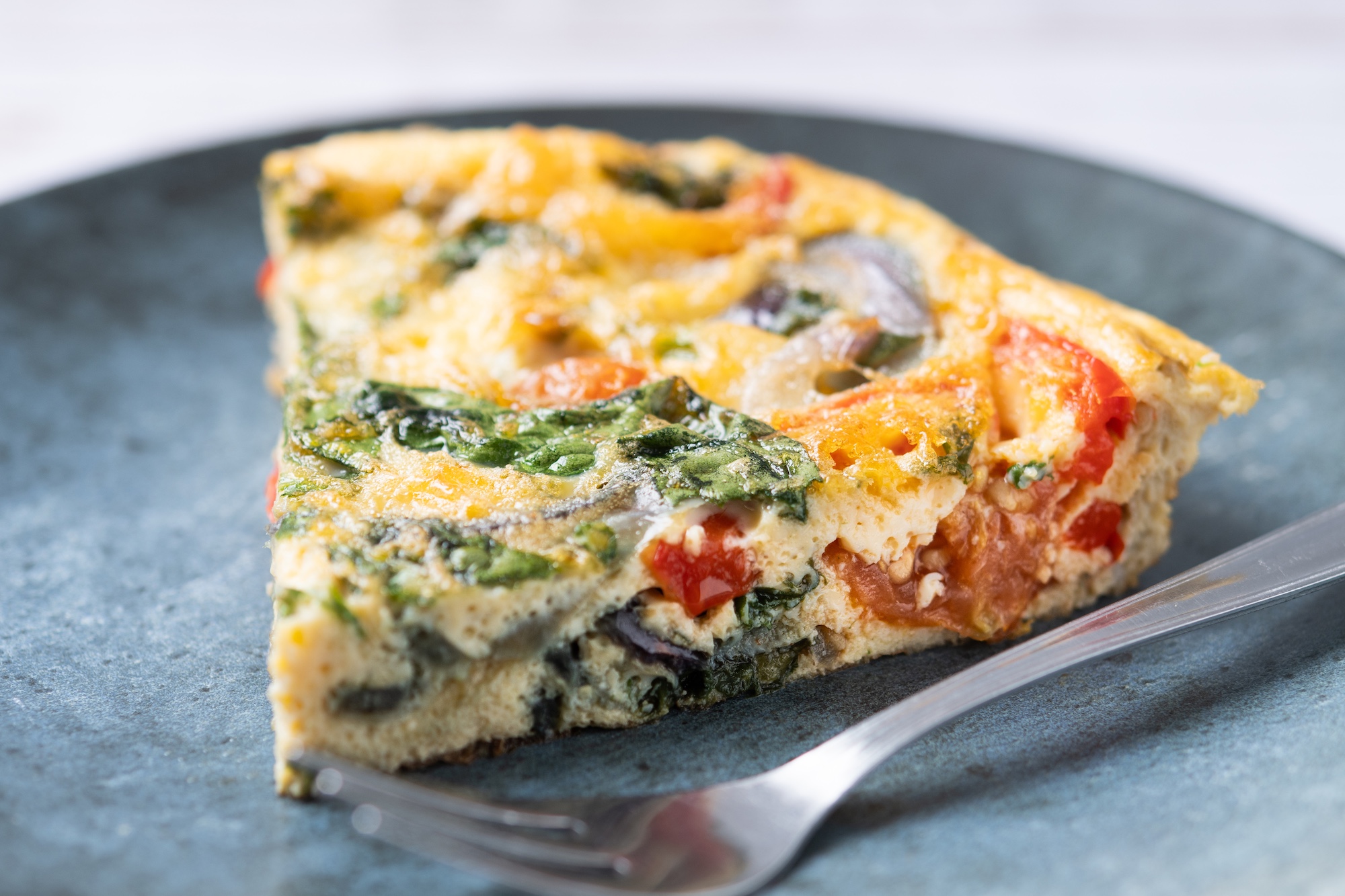 Italian Frittata made with spinach, tomatoes, onion and peppers on white wooden table